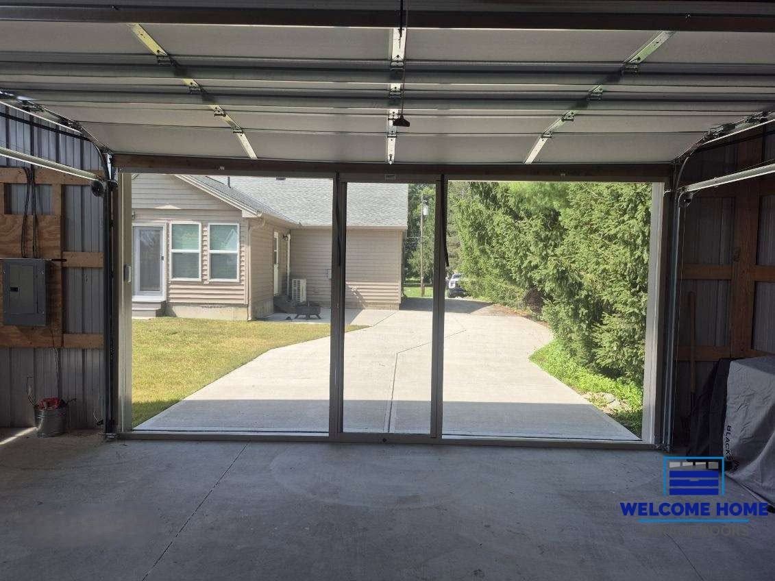 Interior of a garage facing a driveway, lawn, and house through the open door