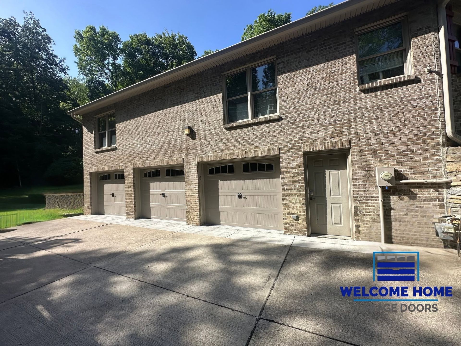 Brick house garage exterior with three white garage doors and a front entry door under blue sky