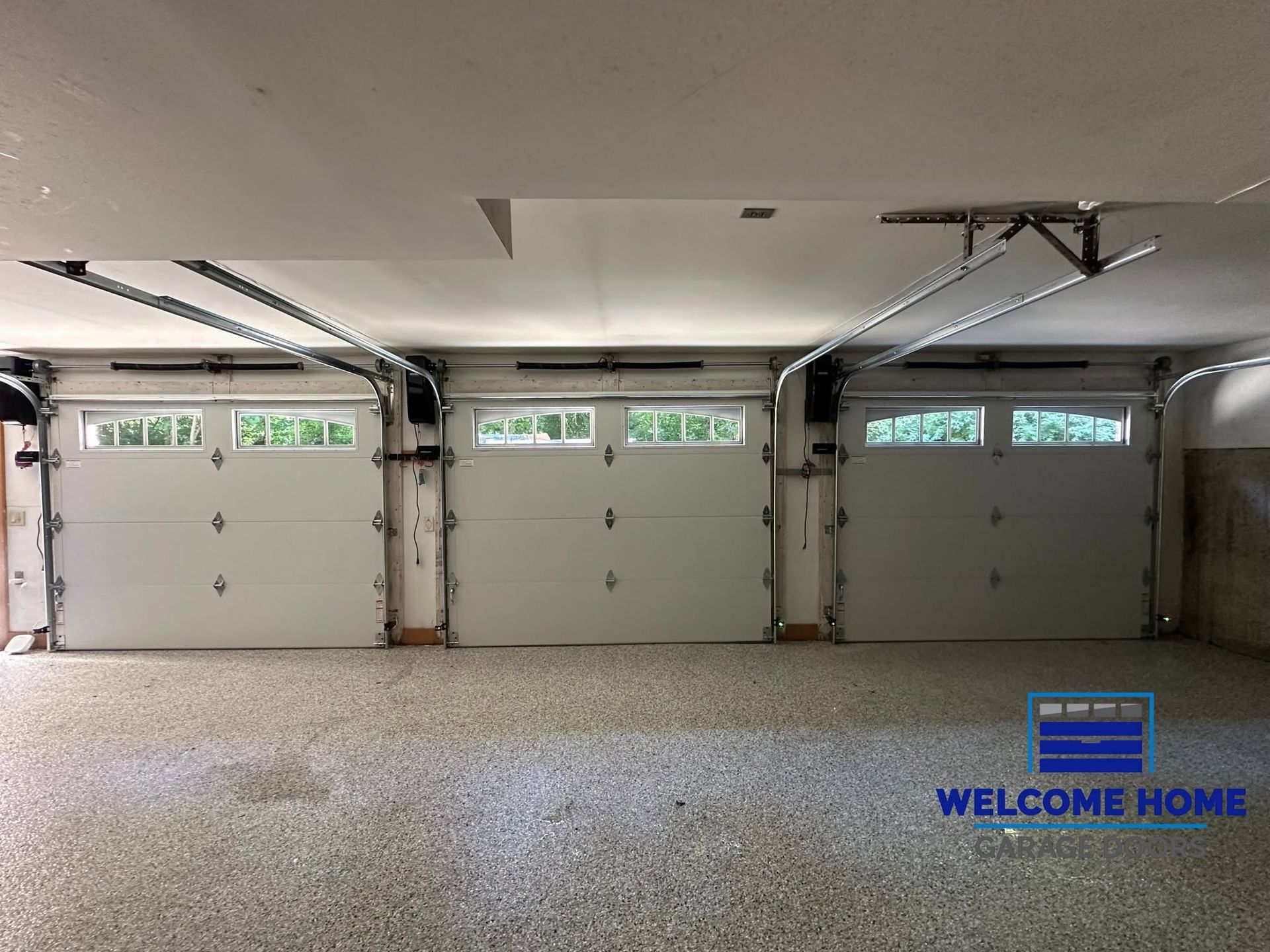 Three-car garage interior with closed white doors and speckled gray floor.
