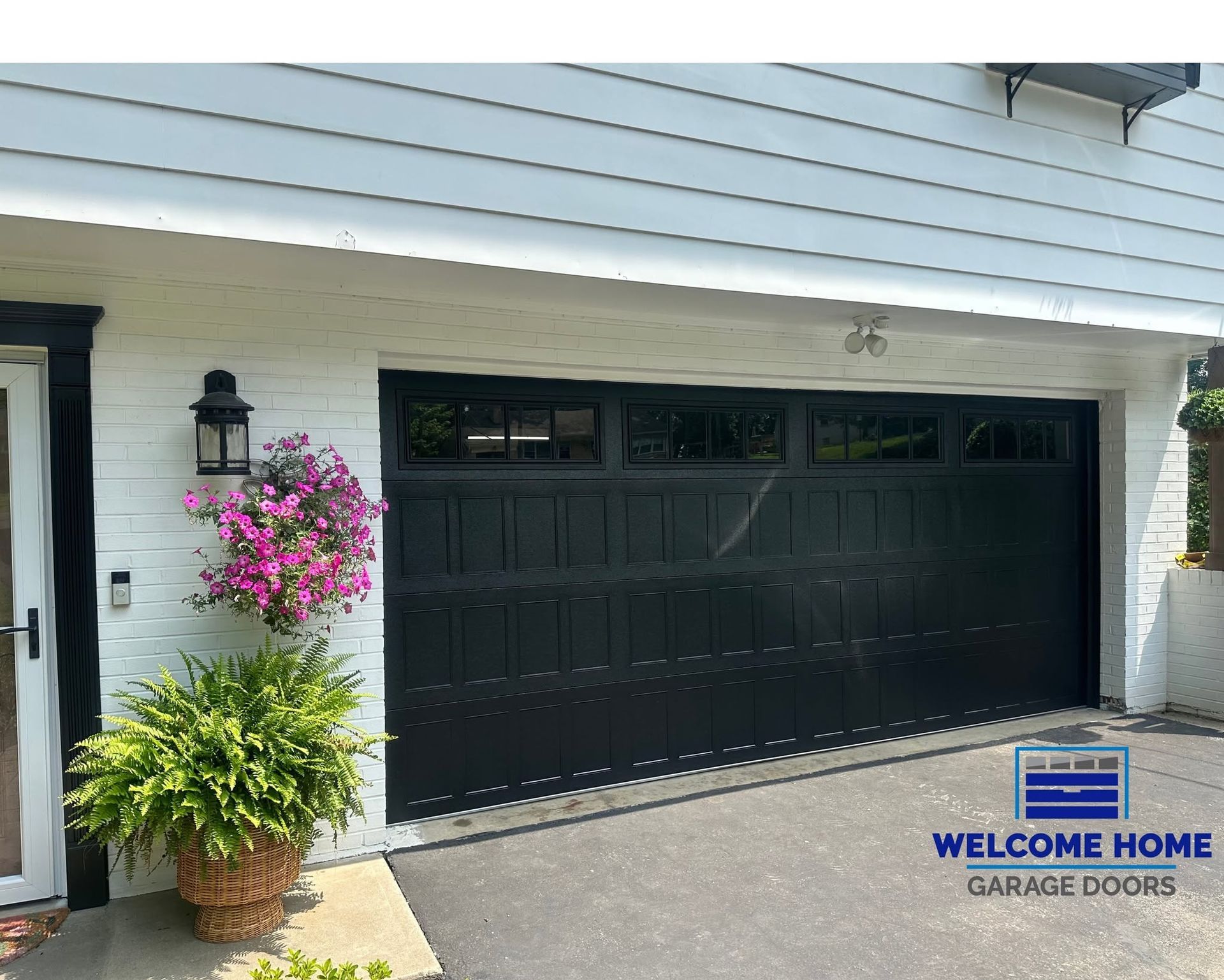 White house with black garage door and pink flowers by the entryway