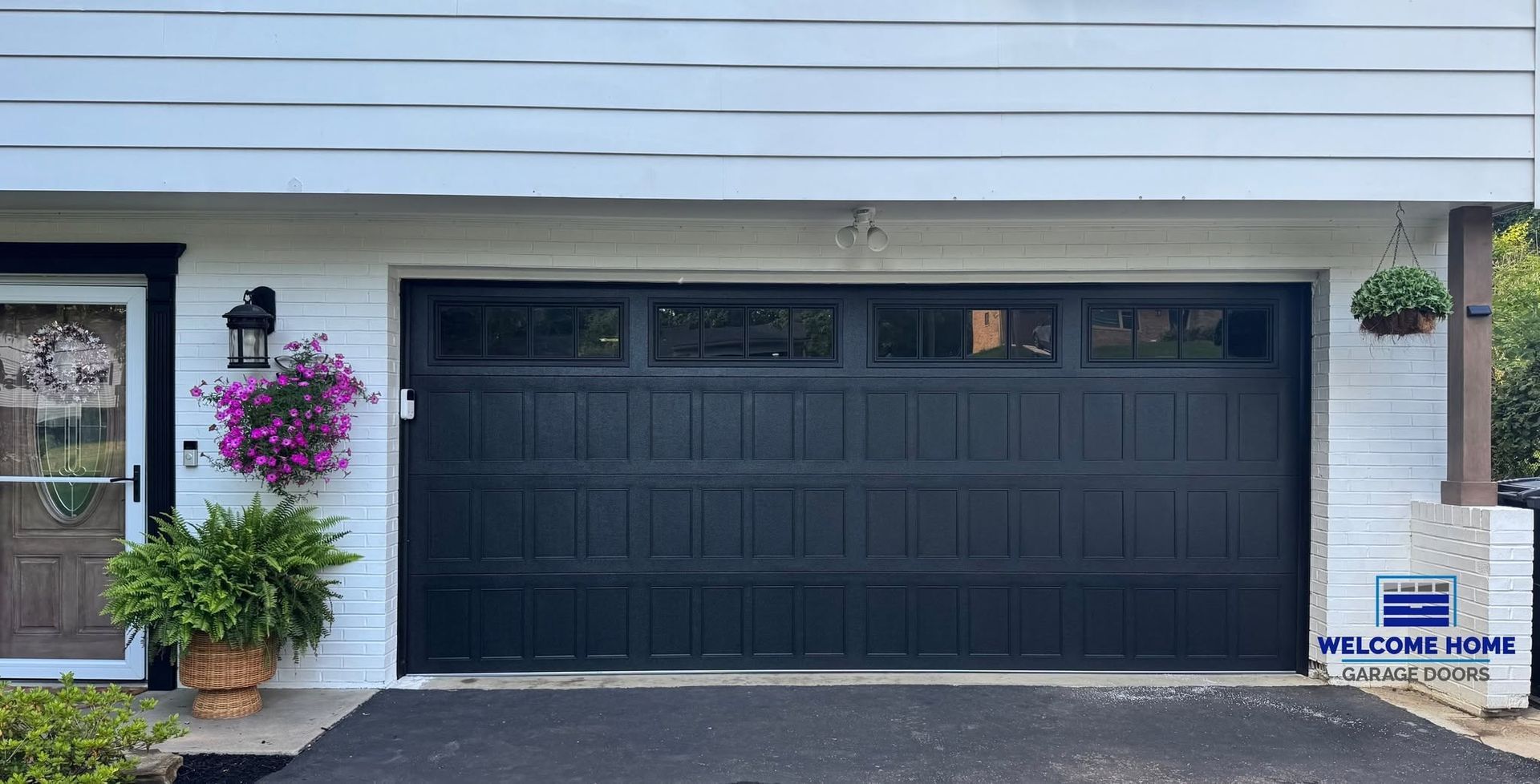 Modern house exterior with a black double garage door, potted flowers, and a front entrance.