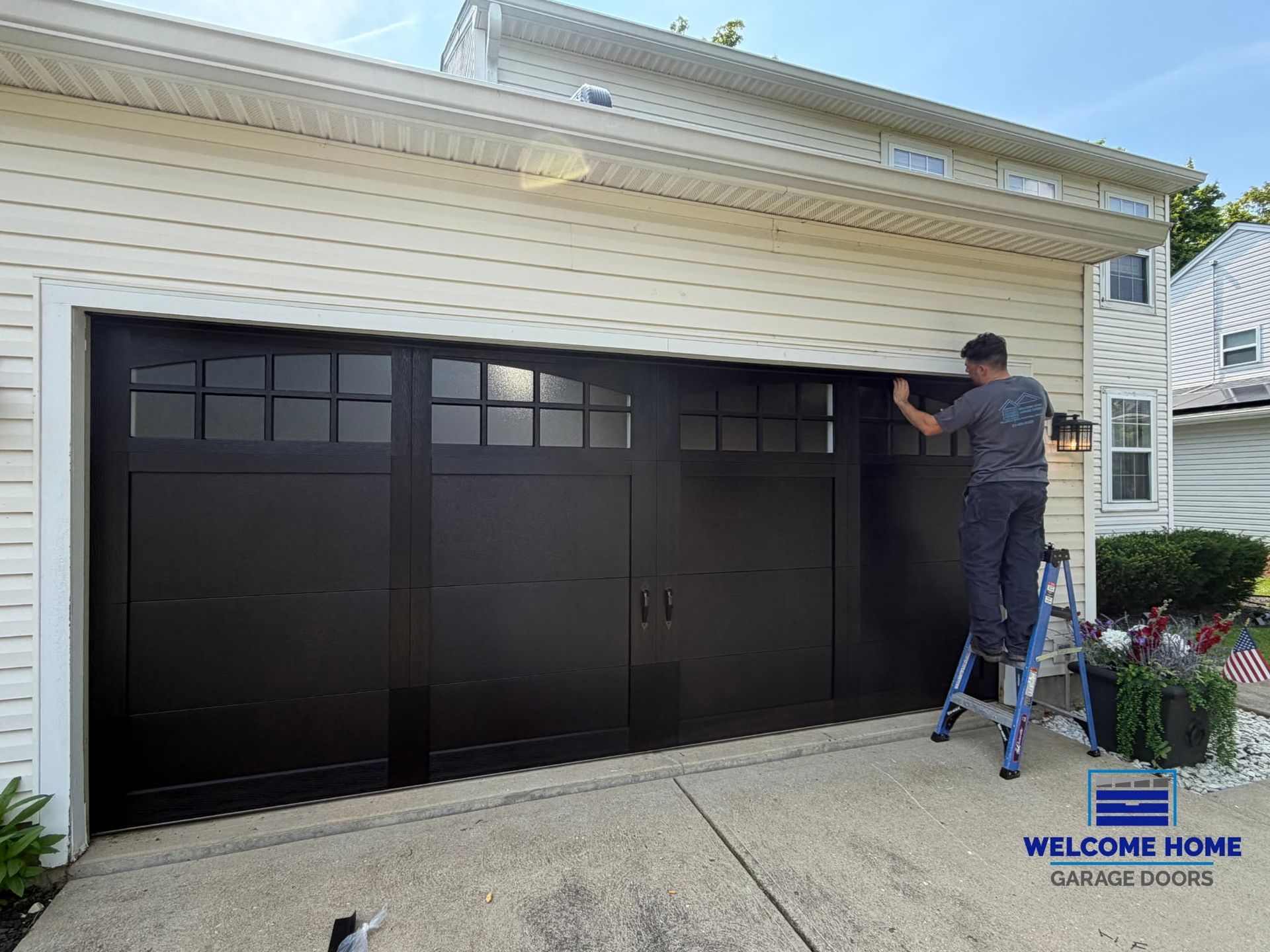 Person painting a black garage door on a white house exterior