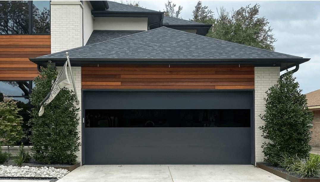 Modern house exterior with a dark gray garage door, wood trim, and landscaped shrubs
