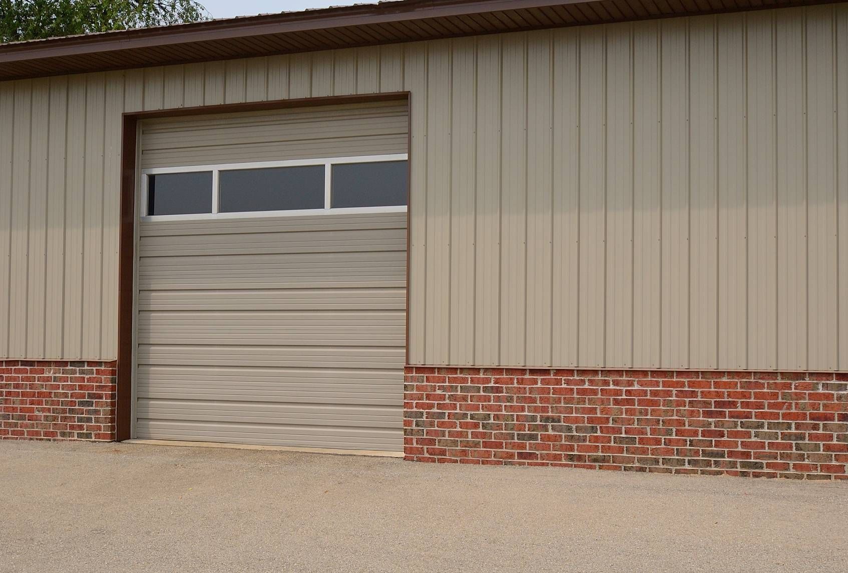 Closed beige garage door with narrow windows in a brick-and-siding building wall