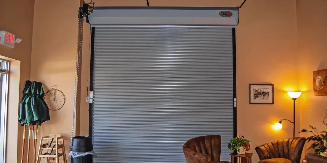 Living room with a closed gray window blind, tan walls, chair, lamp, and wall art