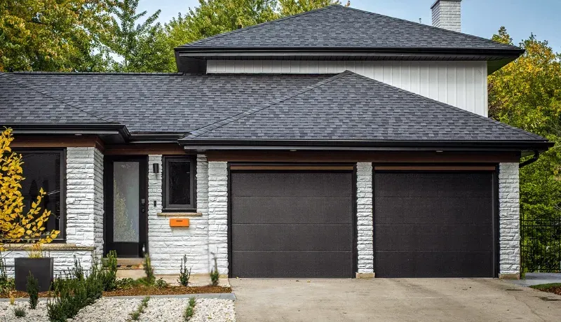Modern two-story house with gray brick, dark roof, and a two-car garage in front of a driveway.