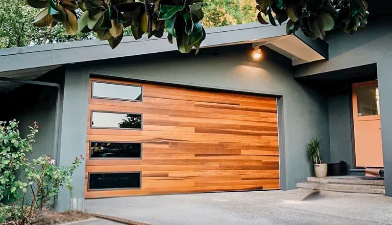 Modern gray house with a wooden garage door, lit entryway, and front steps under trees