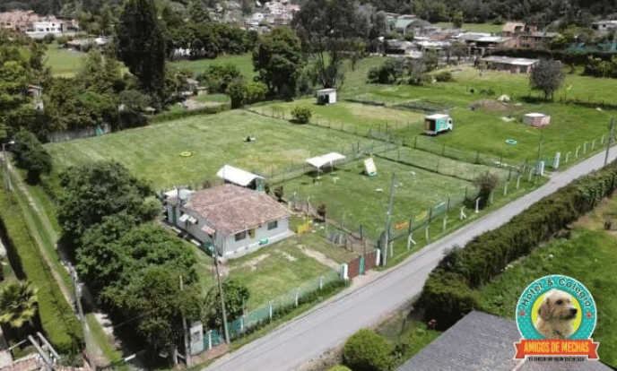 Vista aérea de una propiedad rural cercada, con una pequeña casa, campos de hierba y una carretera en el lindero.