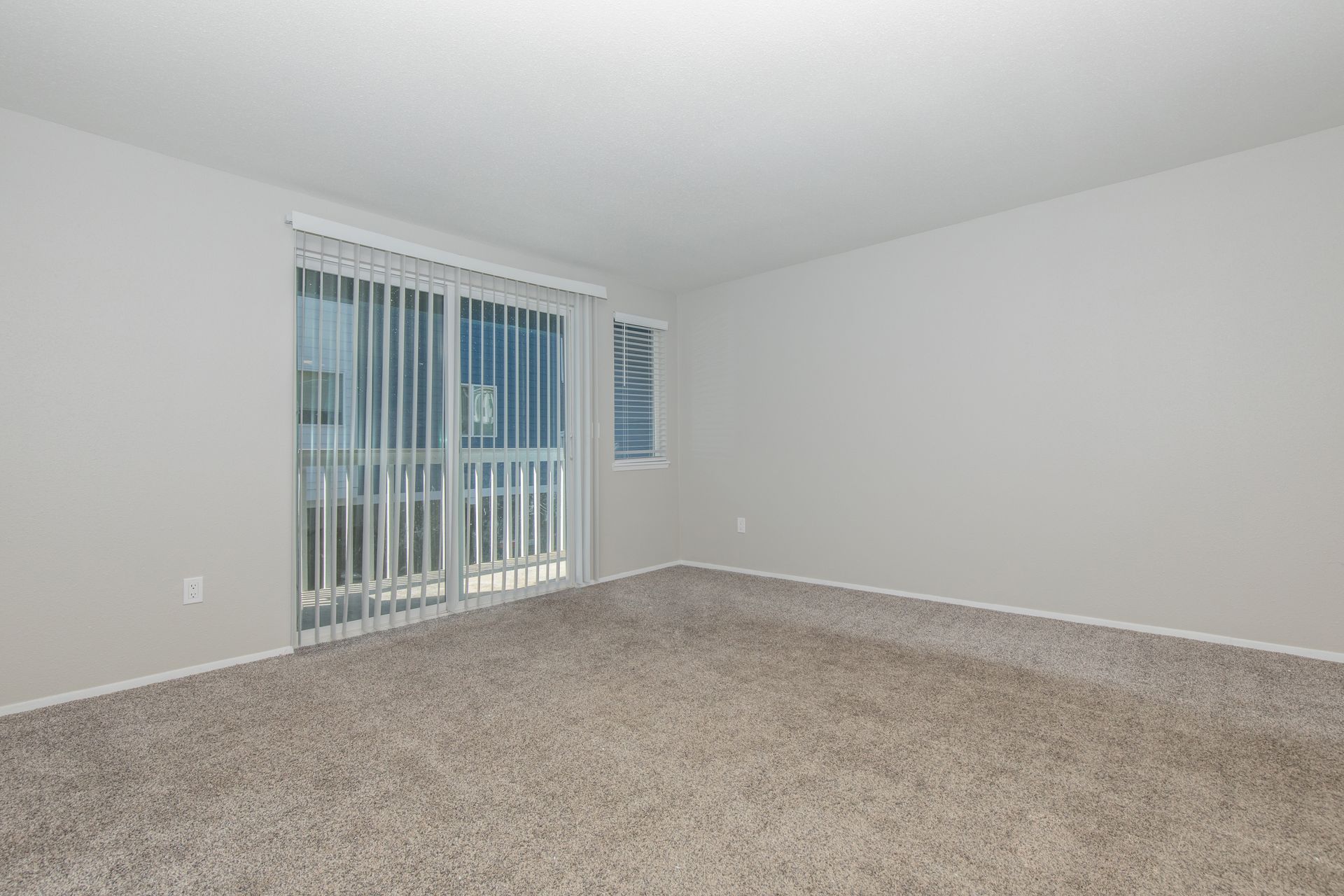 An empty living room with sliding glass doors and blinds.