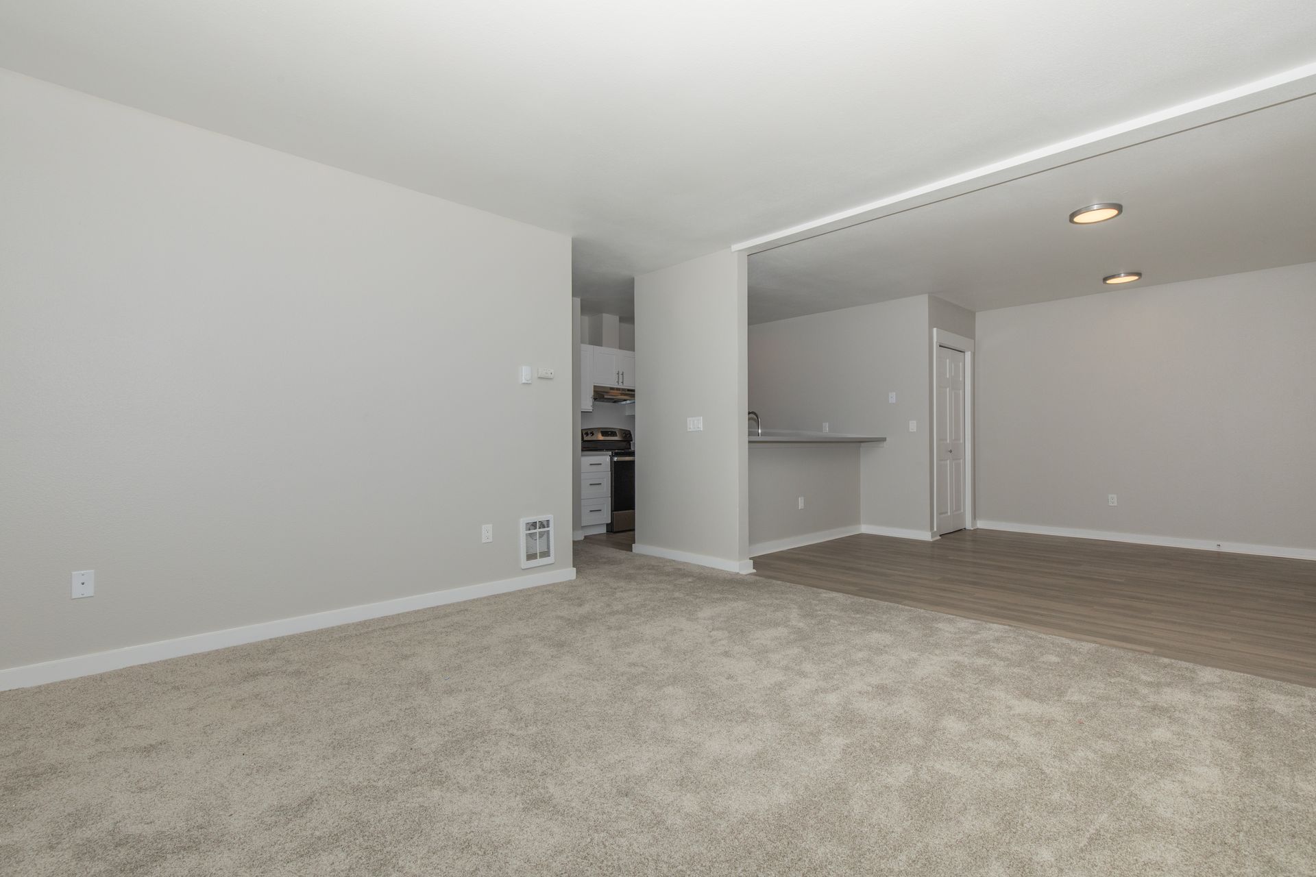 An empty living room with a carpeted floor and white walls.