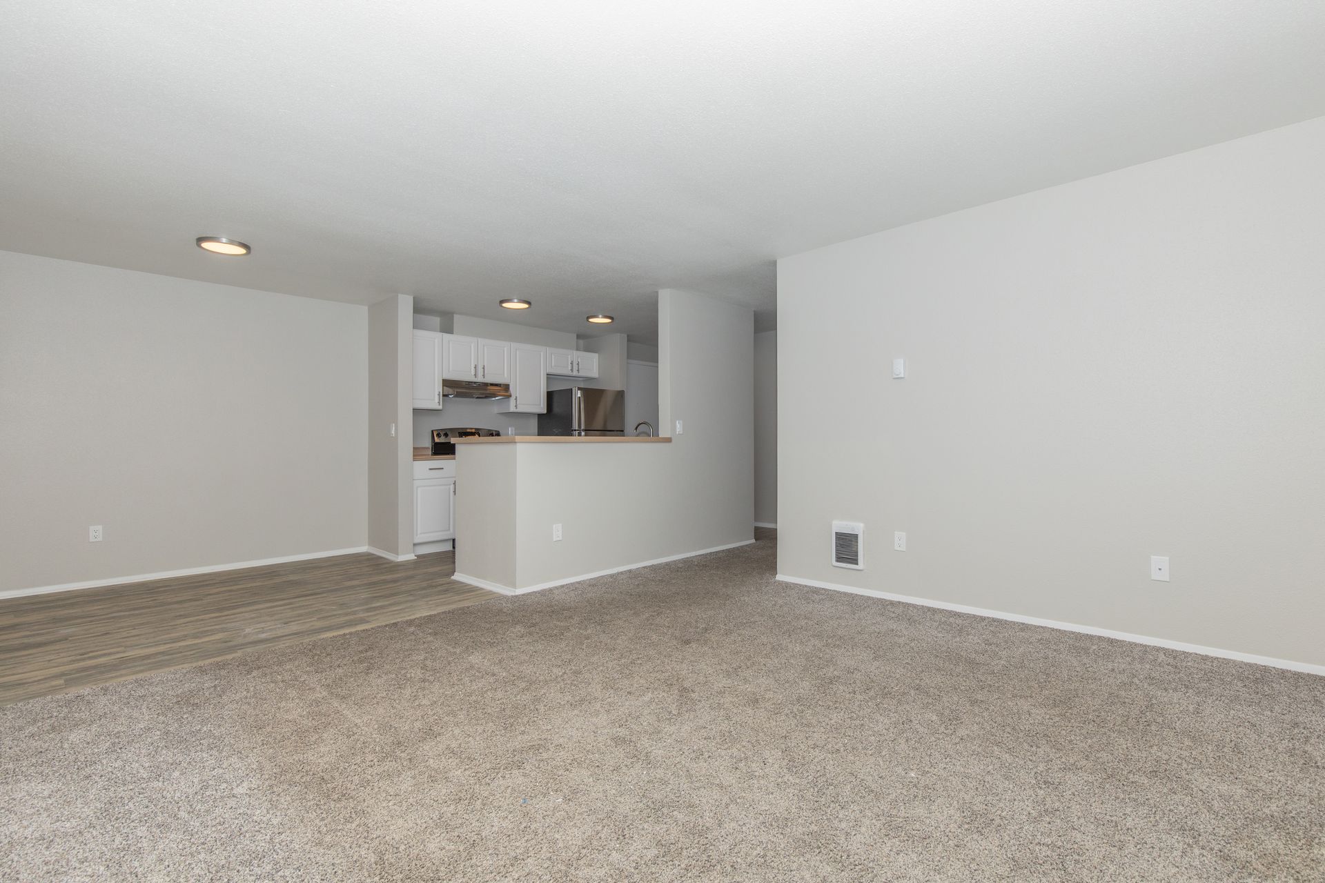 An empty living room with a carpeted floor and white walls.
