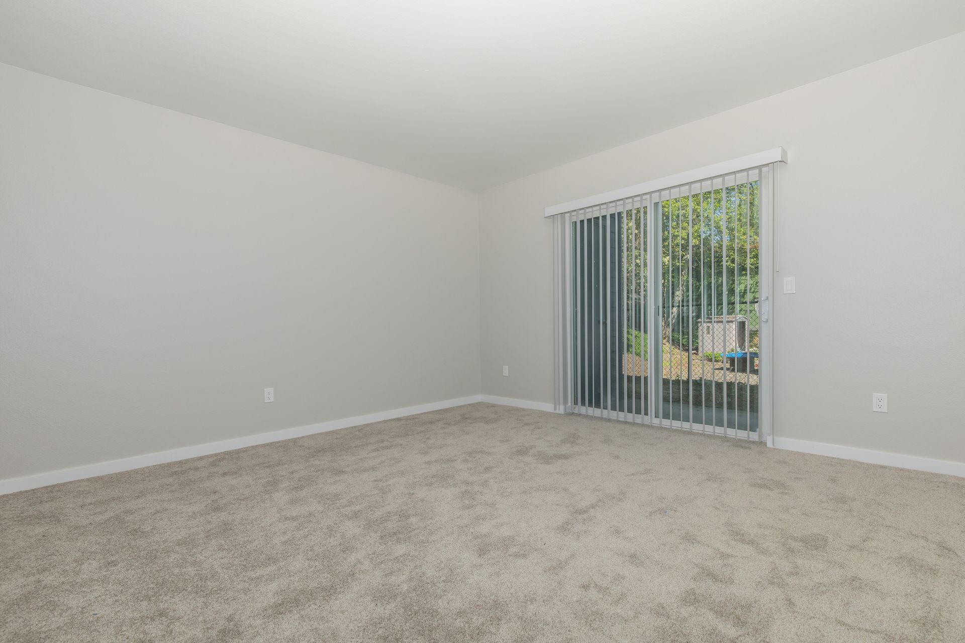 An empty living room with a sliding glass door and blinds.