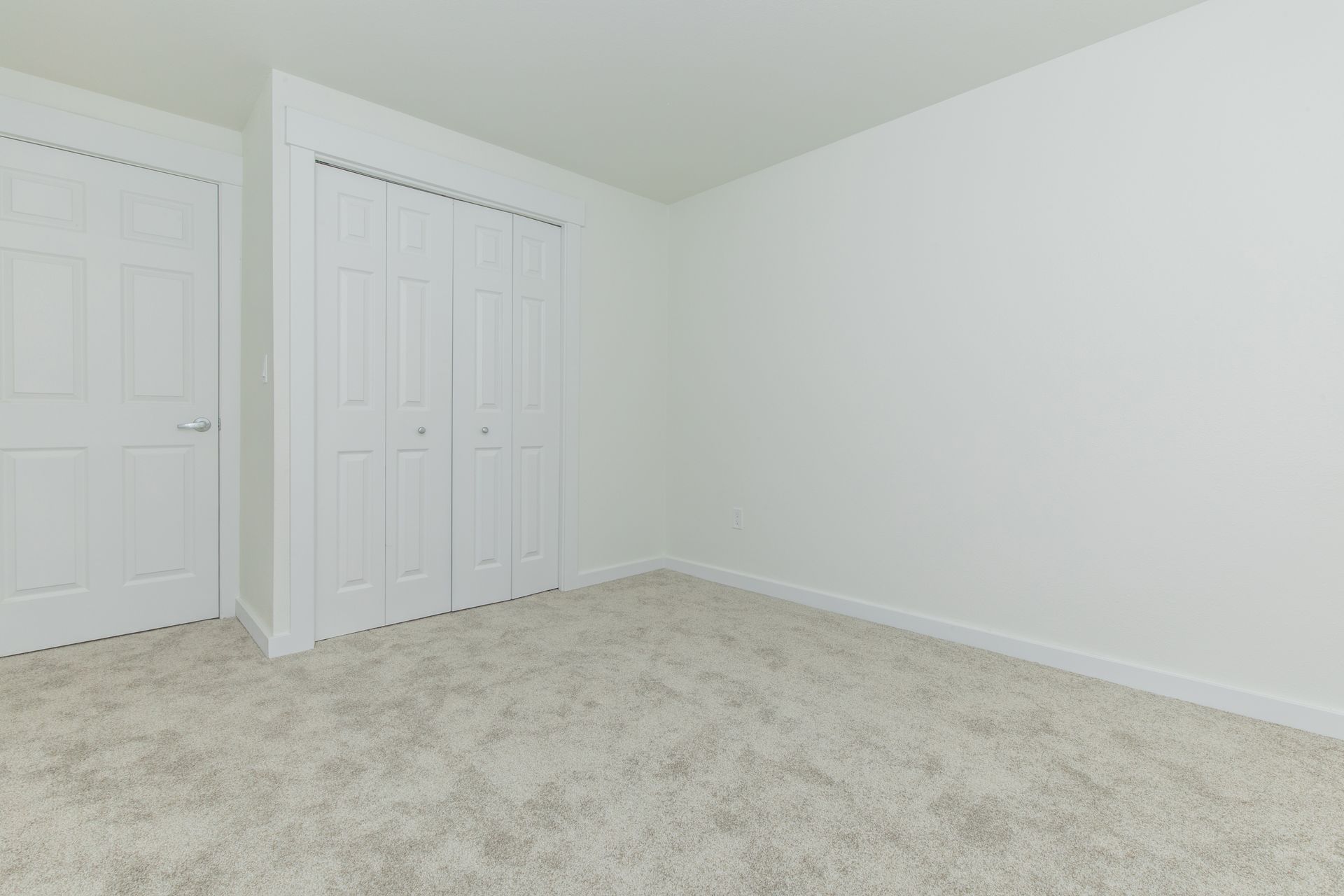 An empty bedroom with a carpeted floor , white walls and closets.