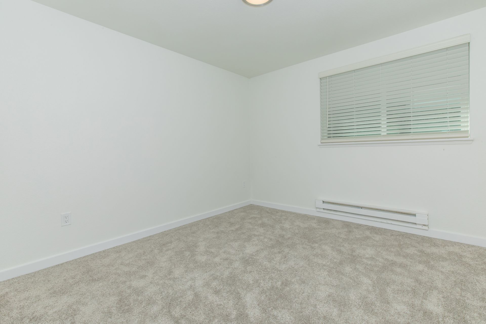 An empty bedroom with a window and blinds.