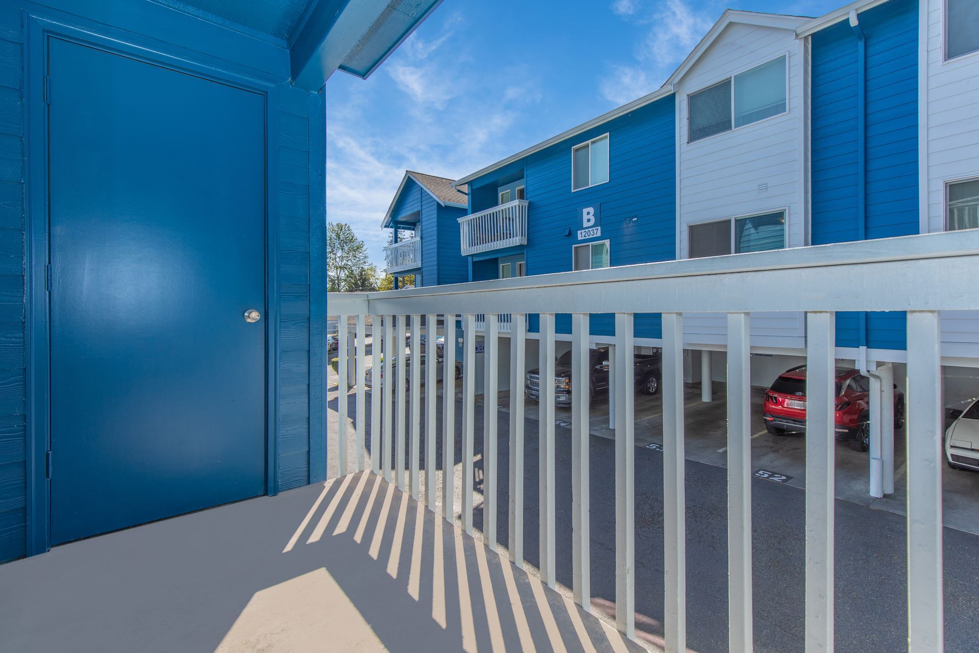 A balcony with a white railing and a blue building in the background.