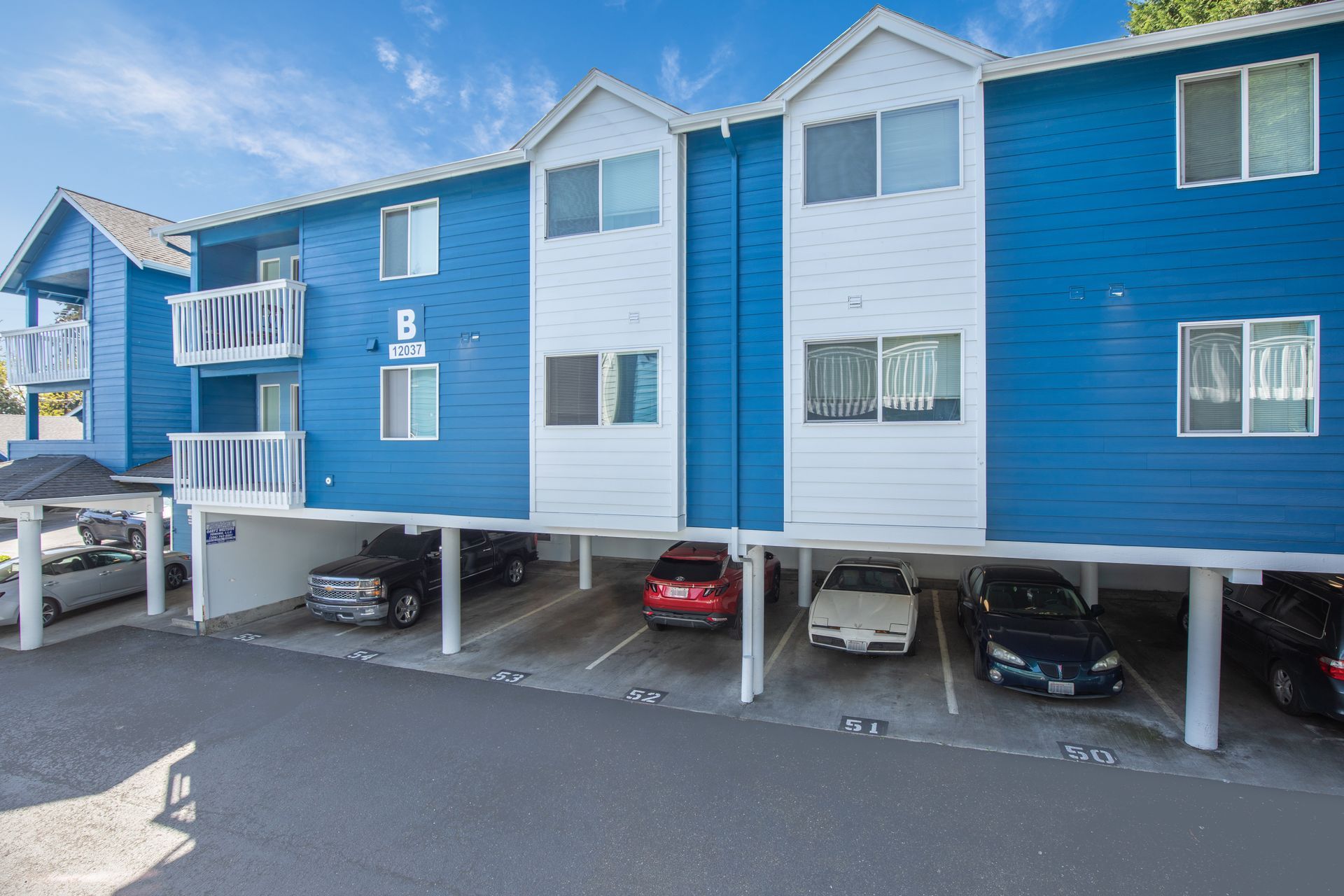 A blue and white apartment building with cars parked underneath it.