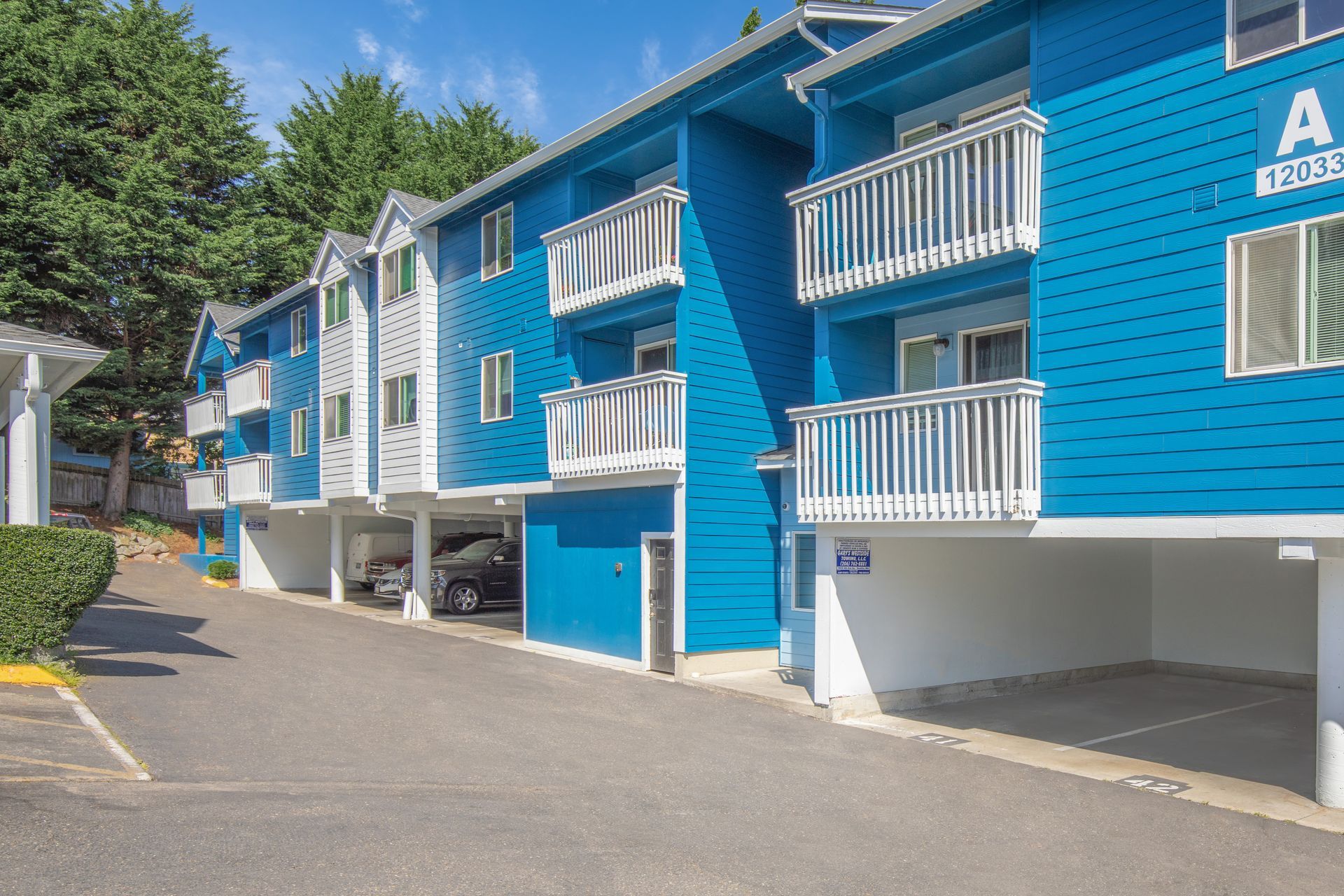 A blue and white apartment building with a parking lot in front of it.