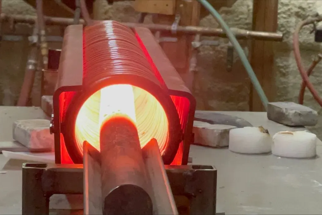 Glowing red-hot metal tube in industrial induction coil showing precise temperature control