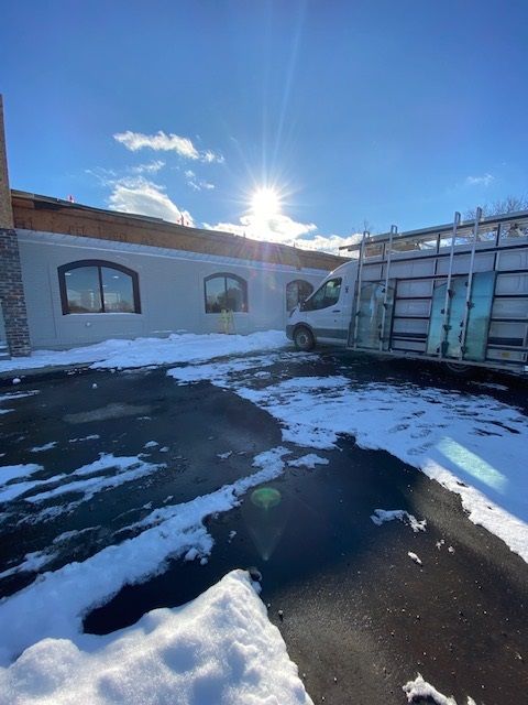 A sunny day with a building being worked on; van parked outside with glass panels, snow on the ground.