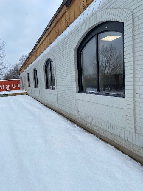 Exterior of a white brick building with arched black-framed windows; snow covers the ground.