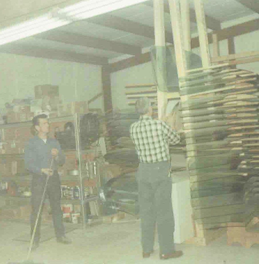 Two men are standing in a room with glass panels on racks.