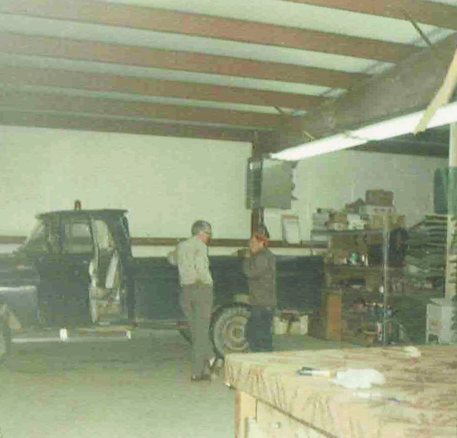 Two men are standing in a garage next to a truck.