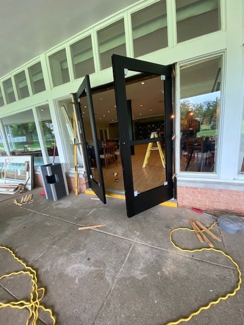 Black doors open, leaning against a building with large windows. Yellow extension cords lie on the concrete.