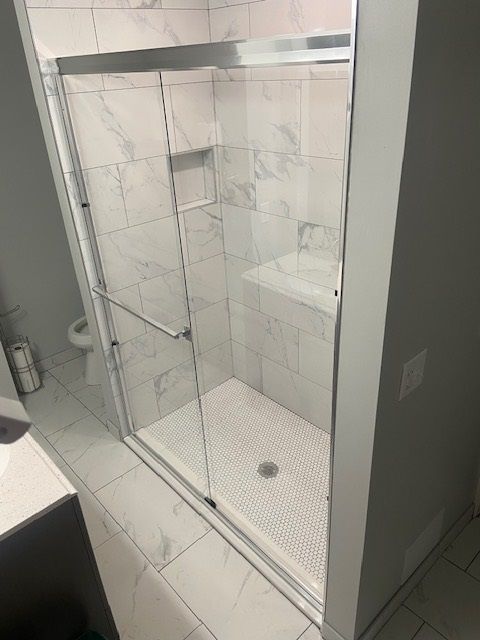 A newly remodeled bathroom with a glass shower and marble-like tile.