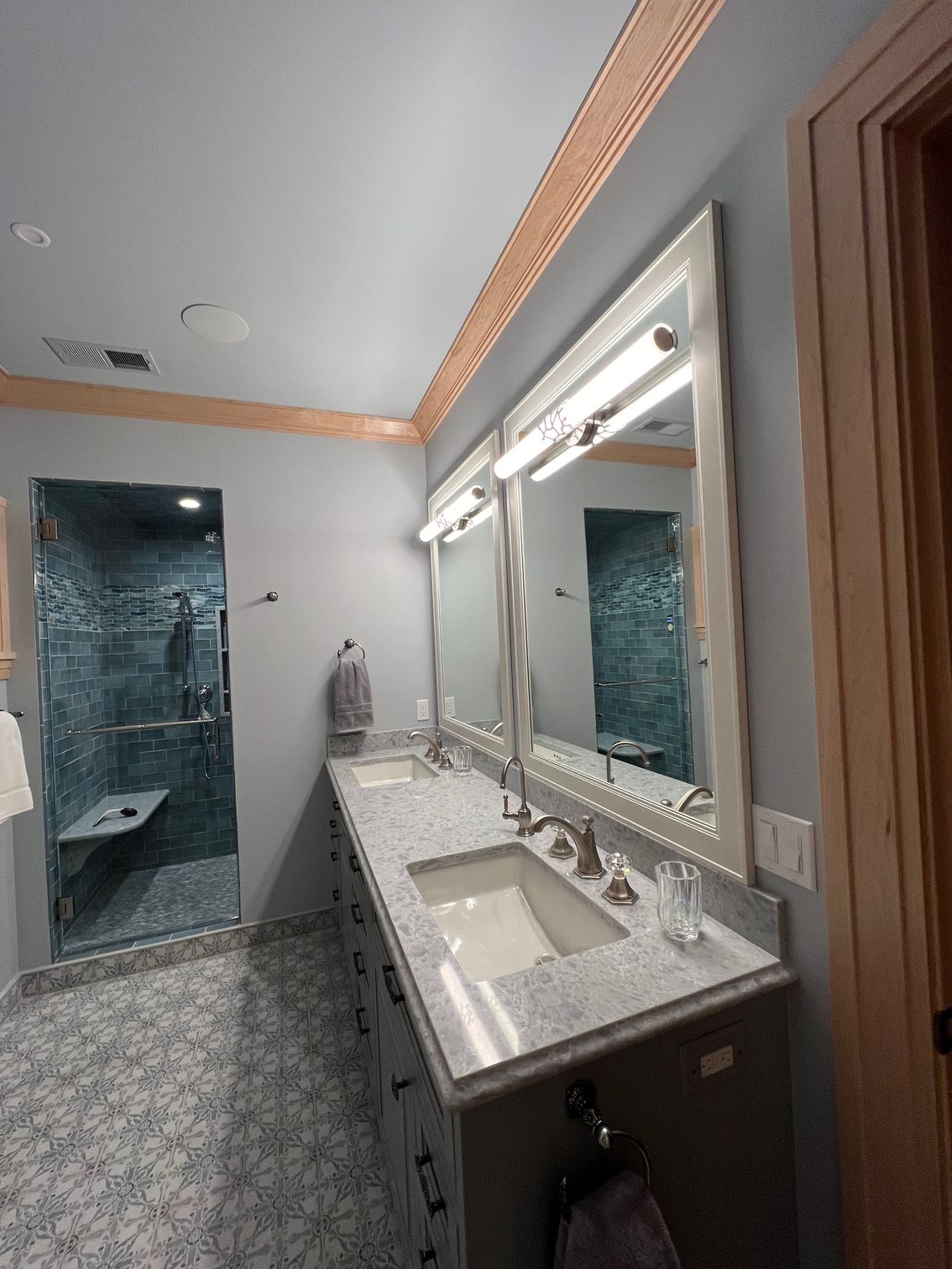 A bathroom with two sinks , two mirrors and a walk in shower.