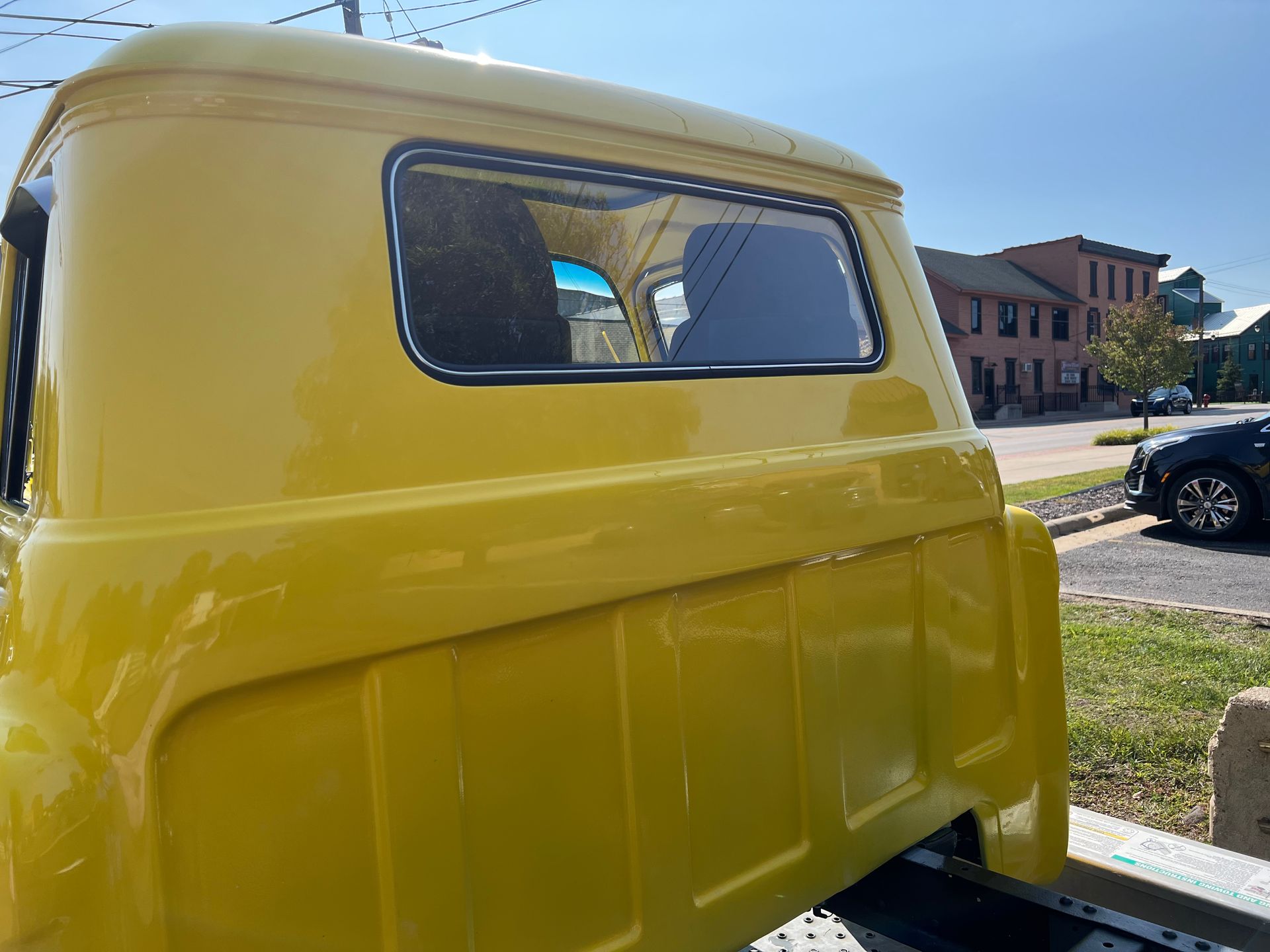 Yellow truck cab with a tinted rear window, parked on a street near a building under a blue sky.