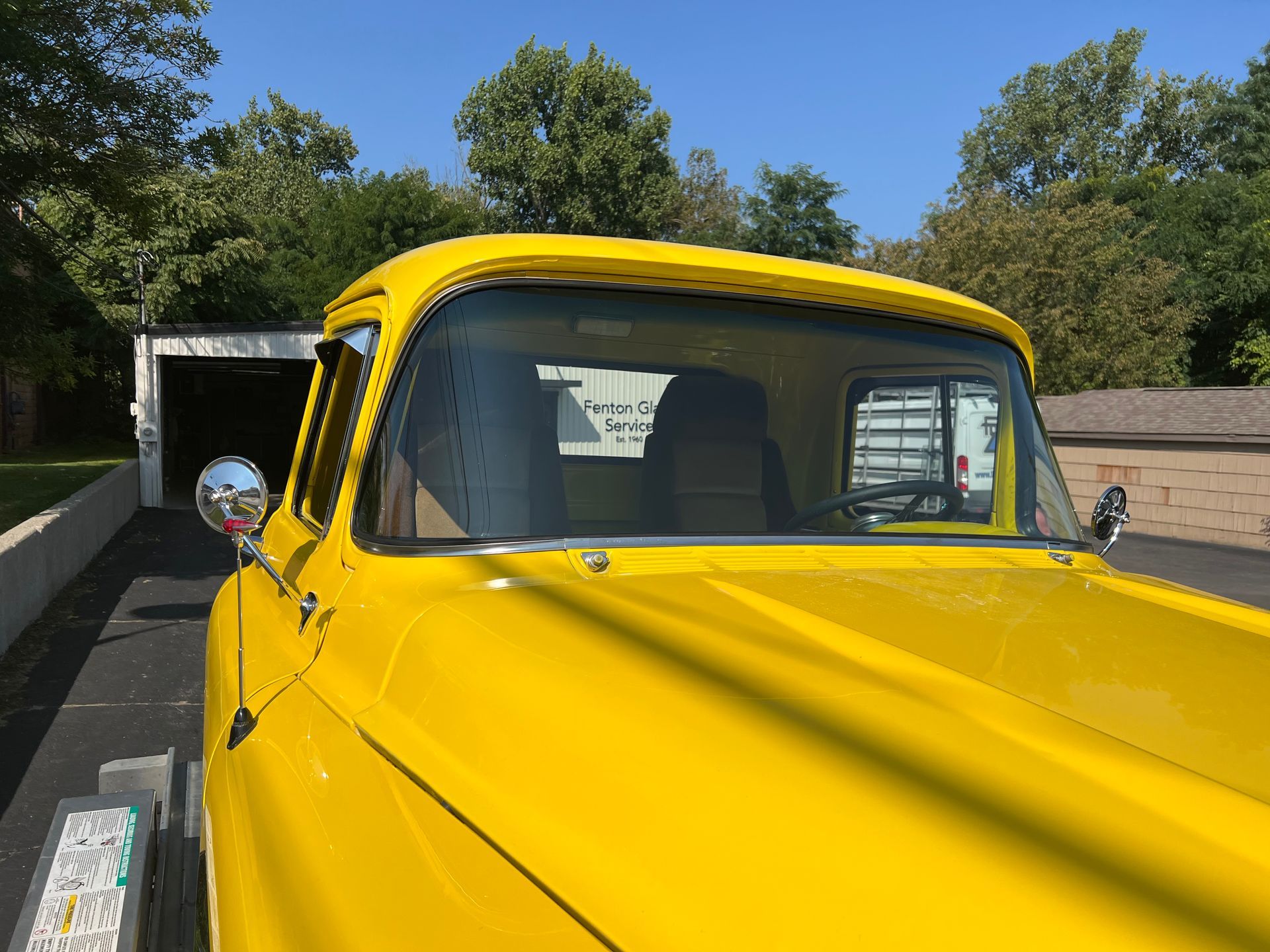 Bright yellow vintage pickup truck parked in front of a garage, sunny day.
