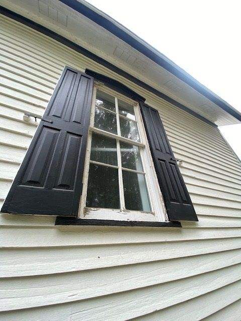 Black shutters flank a white-framed window on a white clapboard wall.