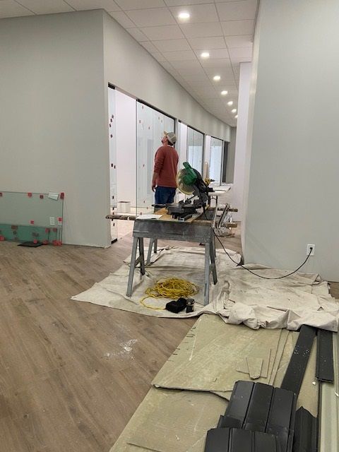 Interior construction in progress with a person, saw, and materials. Light wood flooring, white walls.
