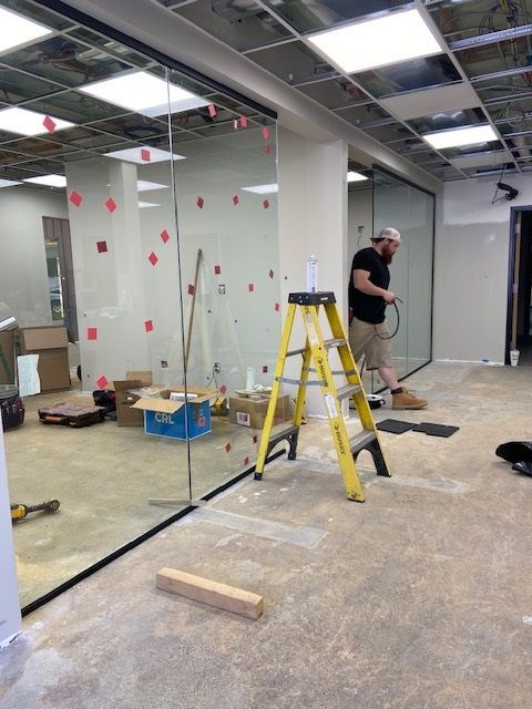 A man works in a construction site with glass walls, a ladder, and boxes on the floor.