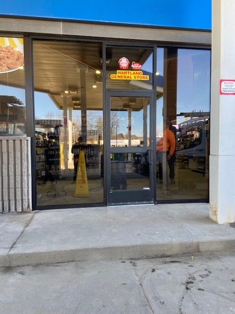 Entrance to a gas station convenience store; glass doors, sign above reads 