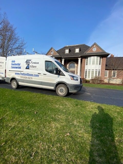 White service van in front of a large brick house on a sunny day. The van says 