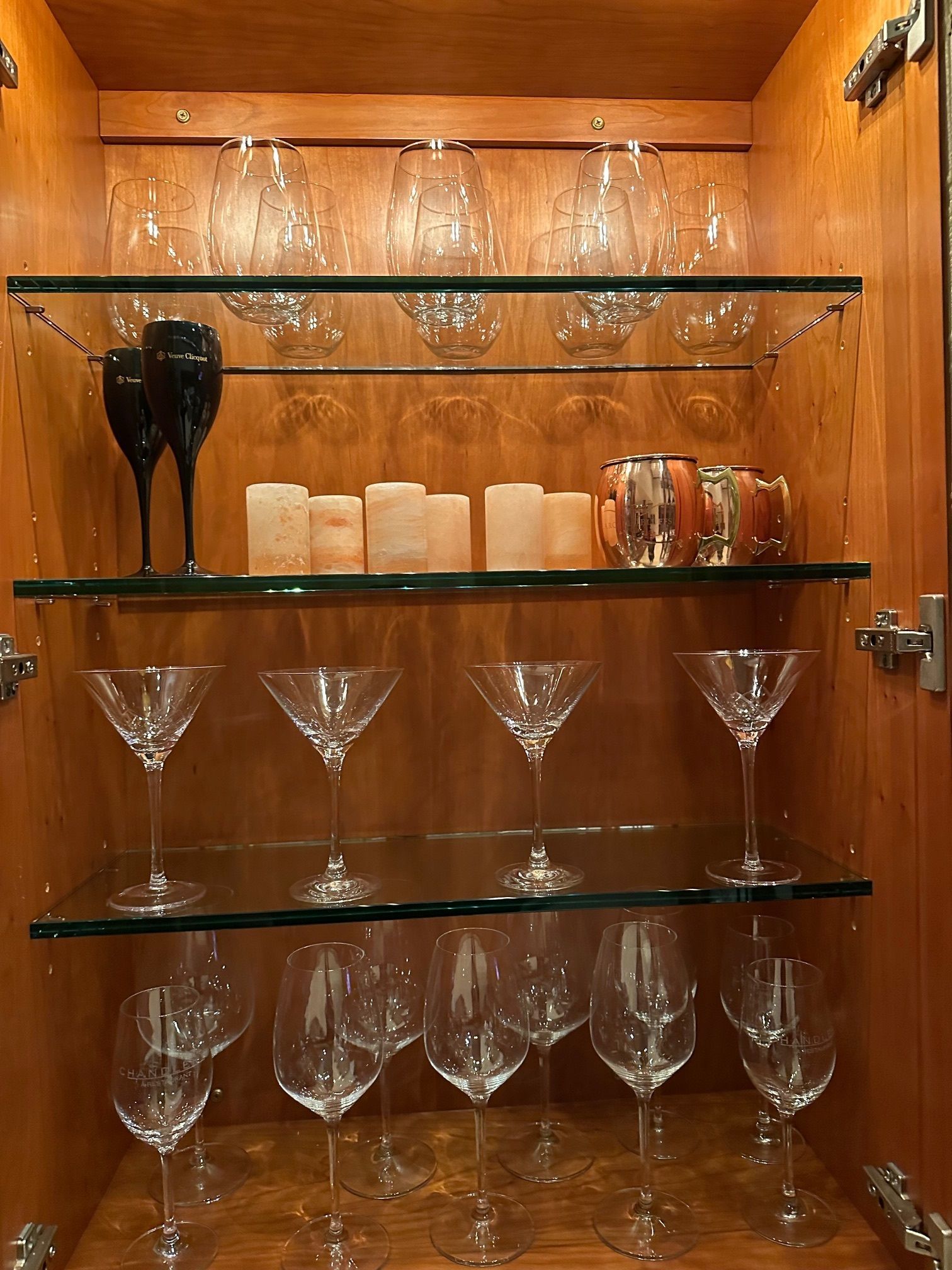 A cabinet filled with wine glasses and candles with glass shelves.