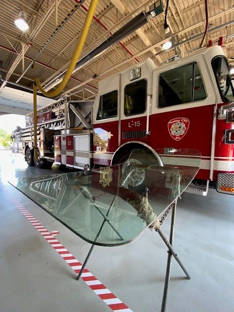 A broken windshield leaning on a stand in front of a fire truck in a fire station.