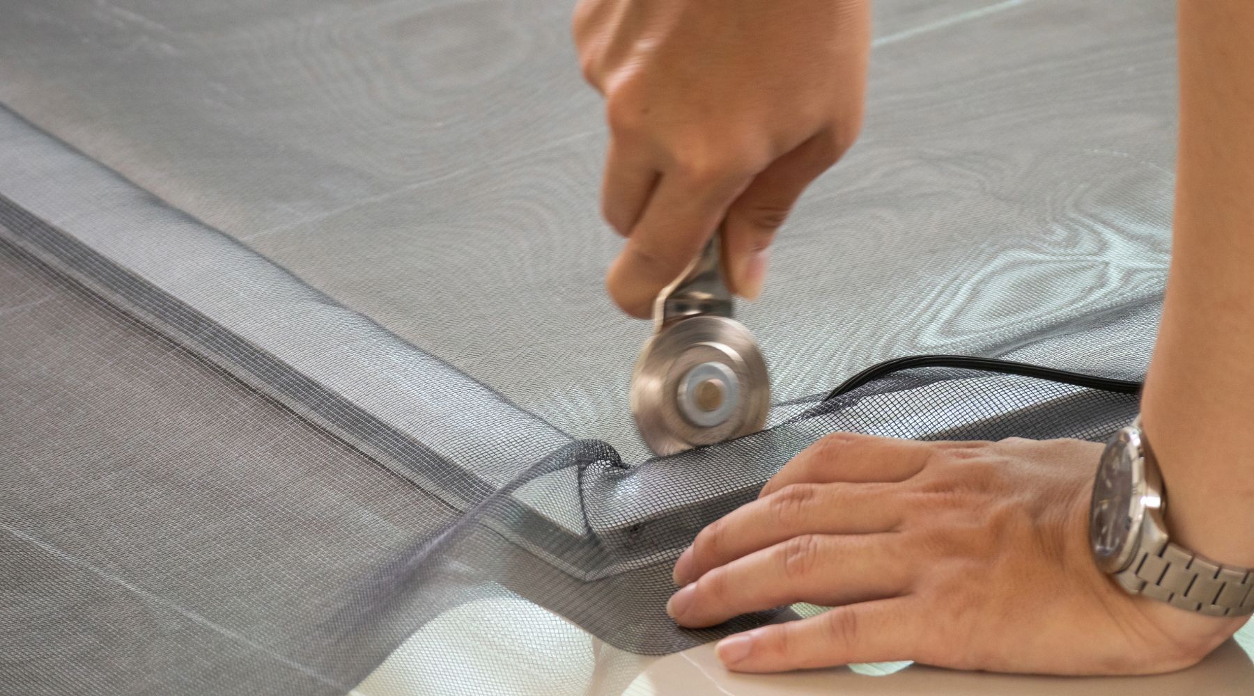 Person using a rolling tool to install screen mesh into a window frame.