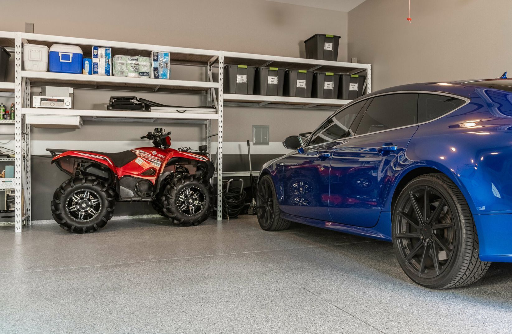 A blue car is parked in a garage next to a red atv.