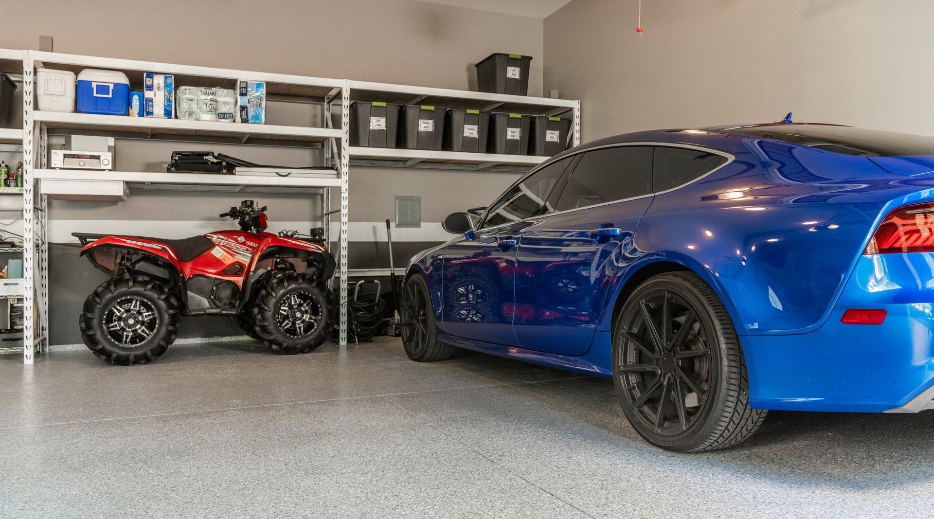A blue car is parked in a garage next to a red atv.