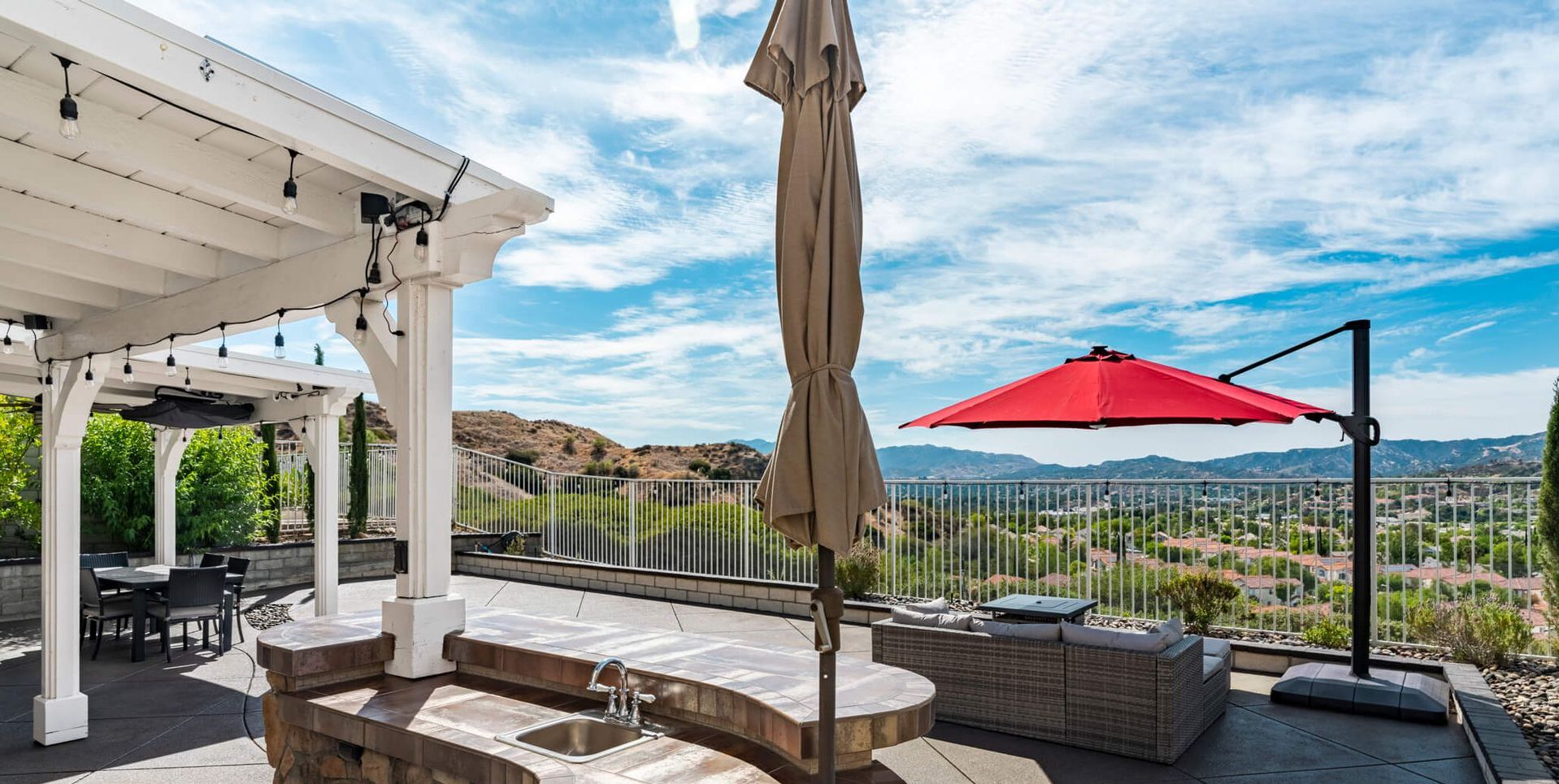 A patio with a red umbrella and a pergola.