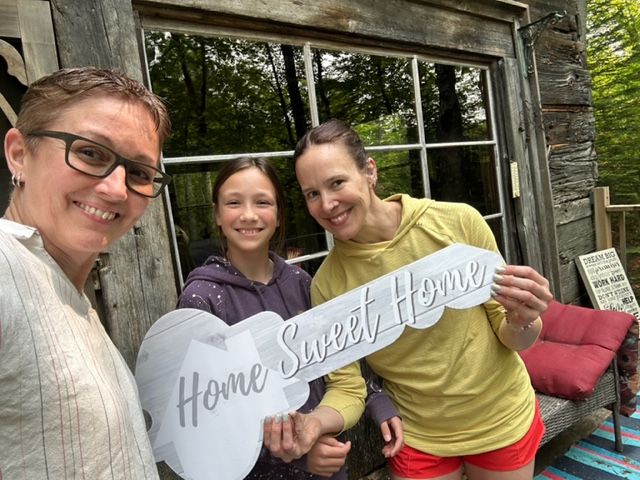 Three people holding "Home Sweet Home" key in front of cabin. Smiling, two adults, a child.