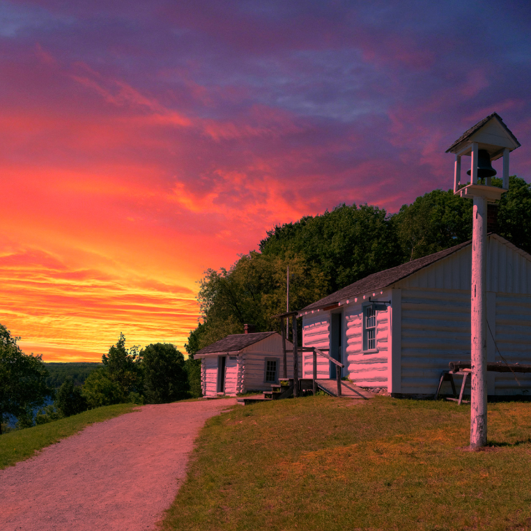Wooden cabins and a bell tower under a vibrant sunset sky.