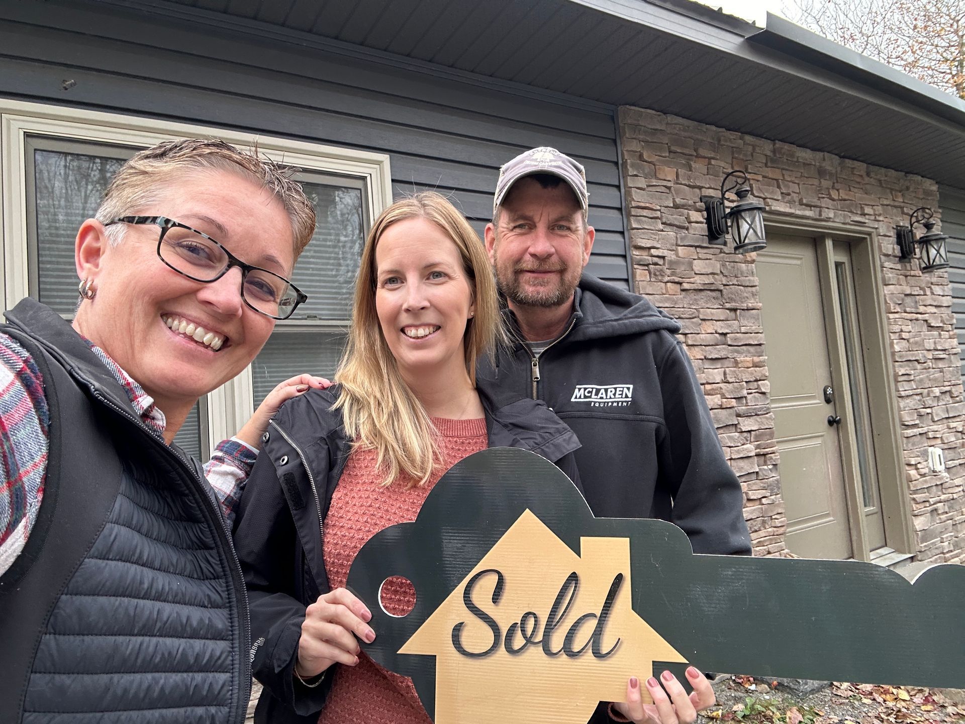 People holding a large "Sold" key in front of a house, smiling.
