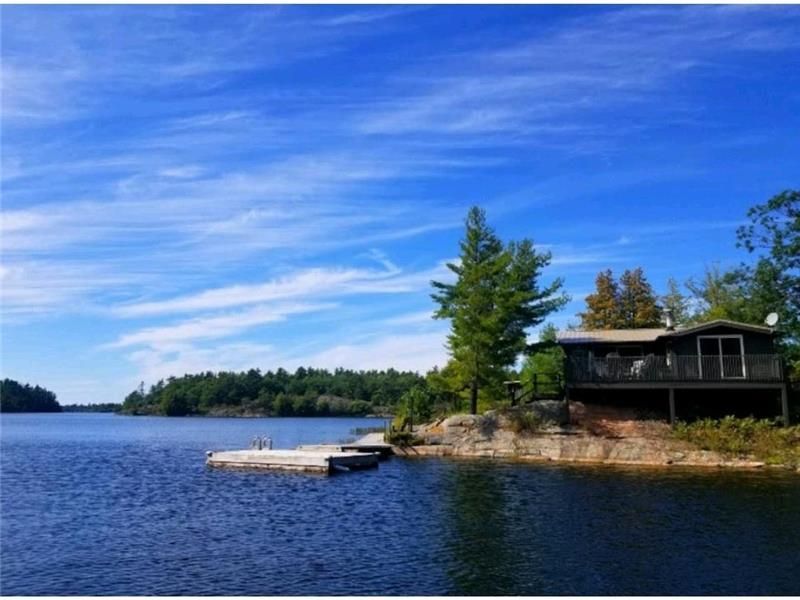 Cabin on a rocky shore of a lake, with a dock and blue sky.
