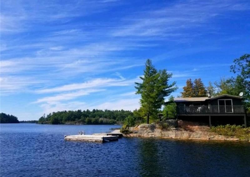 Lakeside cabin with dock on a sunny day. Blue water, sky, and trees.