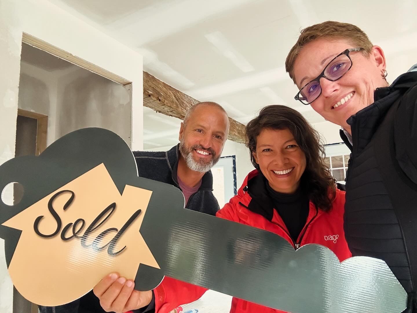Three people holding a large "Sold" key in a new home; smiling.