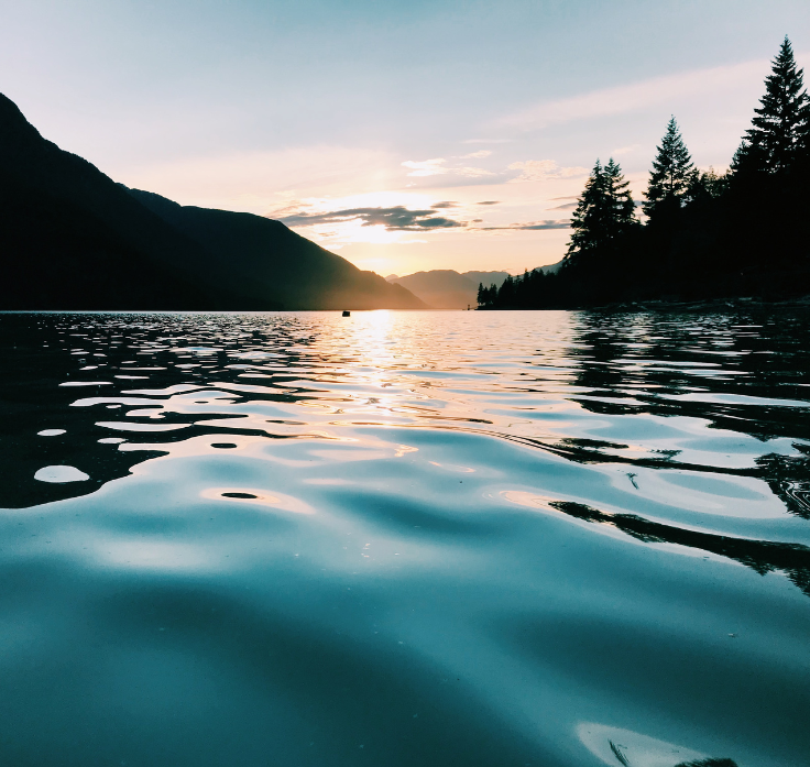 Sunset over a lake with rippling water reflecting the sky; mountains and trees in silhouette.