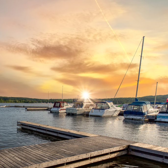 Boats docked at a wooden pier on a lake at sunset; the sun casts a golden glow.